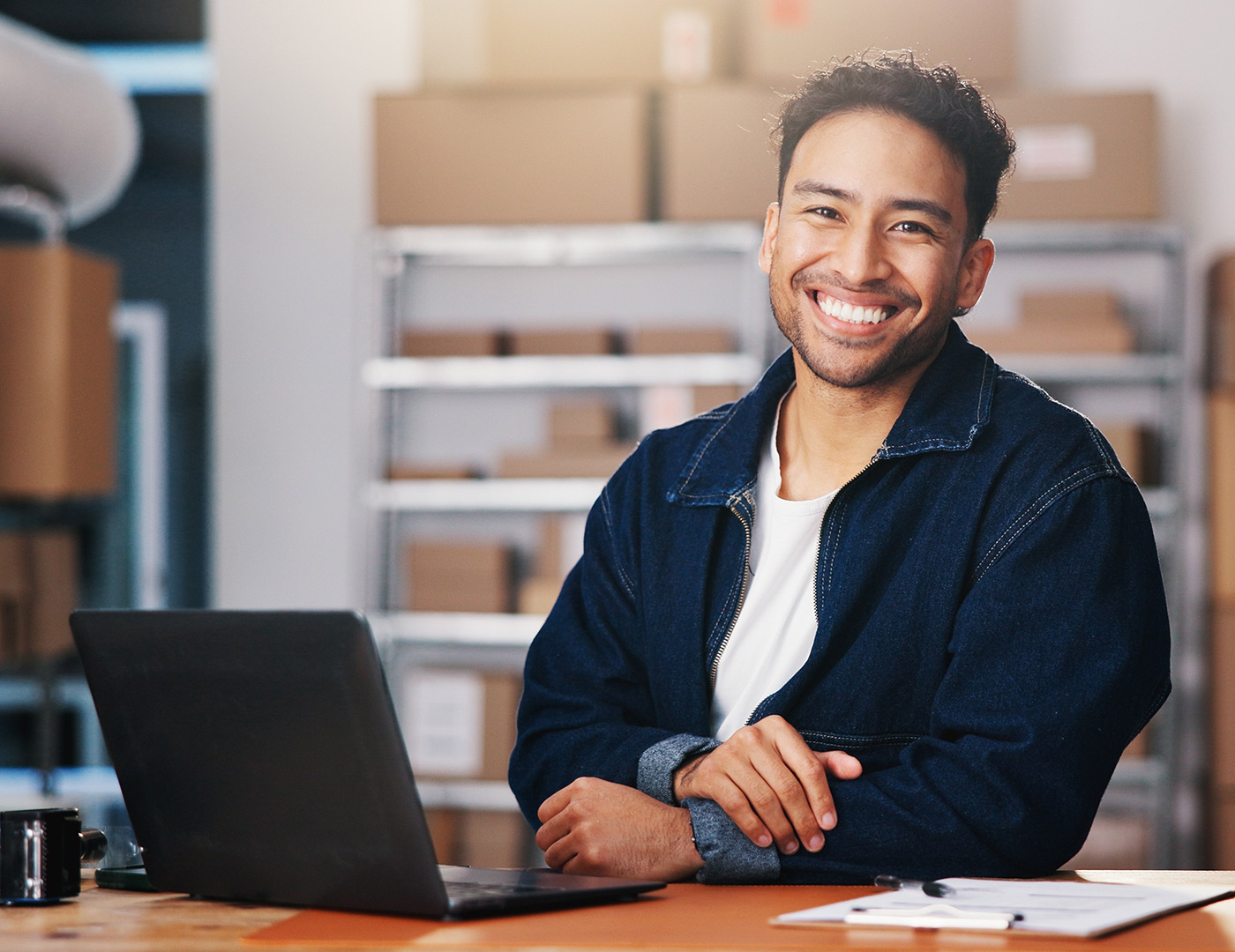 Smiling man with laptop sitting in office, storage boxes in background